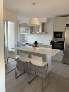 a modern kitchen with stainless steel appliances and white counter tops, along with two bar stools