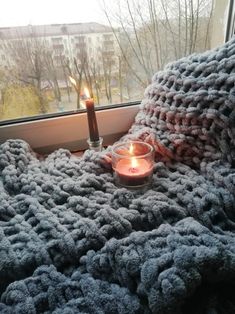 a blanket with a candle on it sitting in front of a window next to a cup