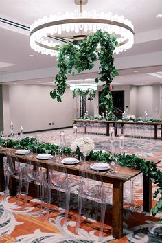 a long table with clear chairs and greenery on it