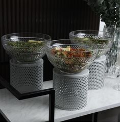 three glass bowls filled with food sitting on top of a table next to vases