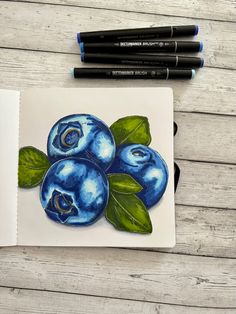 some blueberries are sitting on top of a piece of paper with markers next to it