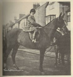 an old black and white photo of a woman sitting on top of a horse in the street