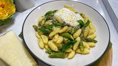 a white plate topped with pasta covered in cheese and greens next to a piece of parmesan cheese