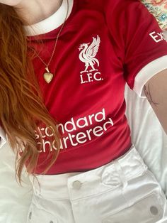 a woman with long red hair wearing a liverpool shirt and white shorts laying on a bed