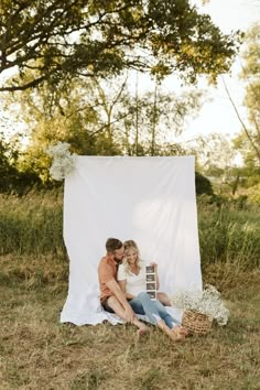 a man and woman sitting on the ground in front of a white backdrop with flowers