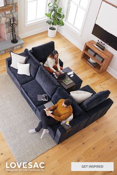 two people sitting on a blue couch in a living room with hardwood floors and large windows