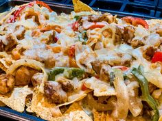 a tray filled with nachos covered in cheese and meat, peppers and onions