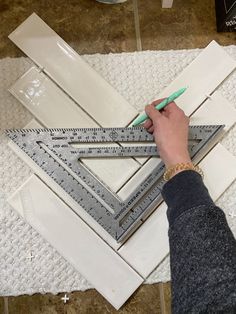 a person is using a ruler to measure the area between two pieces of white tile