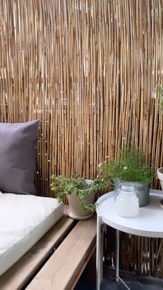 a bed sitting next to a white table with plants on it and a wall behind it