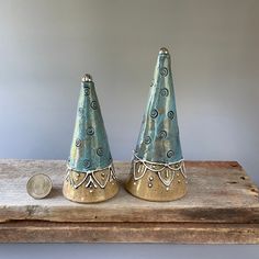 two small ceramic cones sitting on top of a wooden table next to a quarter penny