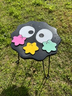 a black table with two eyes and three stars on it sitting in the middle of some grass