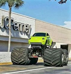 a green monster truck parked in front of a jcaney store with large tires