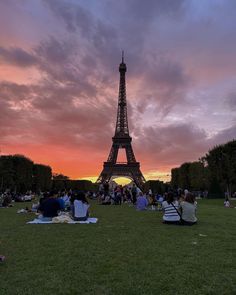 people are sitting on the grass in front of the eiffel tower at sunset