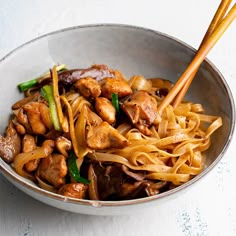 a bowl filled with noodles and meat on top of a white tablecloth next to chopsticks