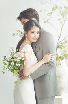 a man and woman embracing each other in front of a tree with white flowers on it