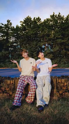 two young men sitting on top of a stone wall next to each other in front of trees