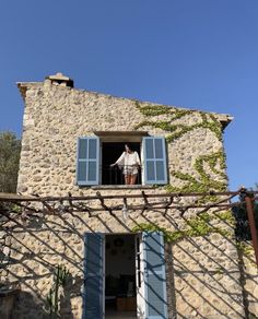 a man standing in the open window of an old stone building with blue shutters