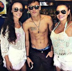 three people standing next to each other in front of a bar wearing sunglasses and one man with tattoos on his chest