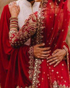 a woman in a red and gold bridal outfit hugging her husband on the forehead