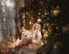 a woman sitting in front of a christmas tree holding a teddy bear