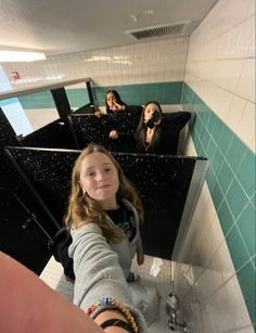 a woman taking a selfie in a bathroom with three other women sitting on the sinks