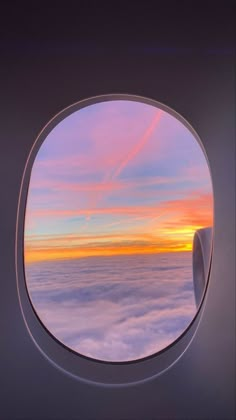 an airplane window with the view of clouds below it and a sunset in the distance