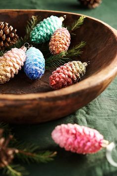 some pine cones are sitting in a wooden bowl on a green tablecloth with pink and blue ornaments