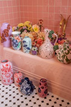 many different vases and flowers are sitting on the shelf in front of a tiled wall