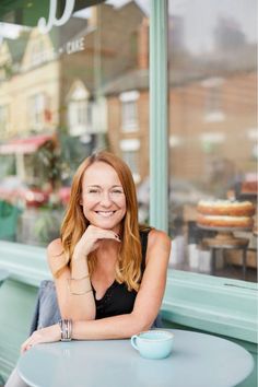 a woman sitting at a table in front of a doughnut shop smiling for the camera