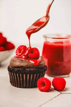 chocolate cupcakes with raspberries and sauce being drizzled on top