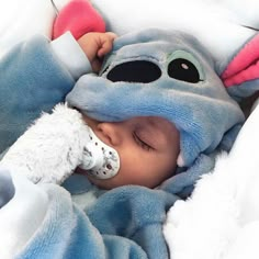 a baby sleeping in a blue and white blanket with a stuffed animal on it's head