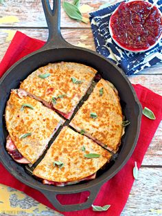 an iron skillet filled with quesadillas cut into four sections and sauce on the side