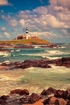 a lighthouse on top of a small island in the middle of the ocean with waves crashing around it