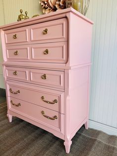 a pink dresser with gold handles and knobs in a room next to a wall