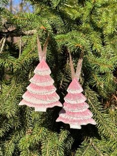 two pink christmas trees hanging from a tree branch with pine needles in the foreground