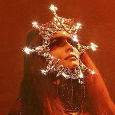 a woman with long hair wearing a crown on her head and lights in the background