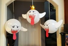 three white balloons with faces and mouths hanging from strings in front of a door,