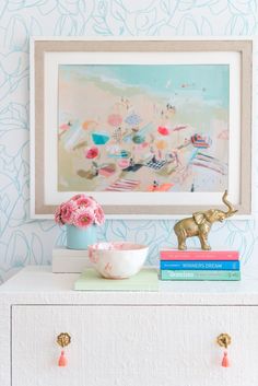 a white dresser topped with books and a vase filled with flowers next to a painting