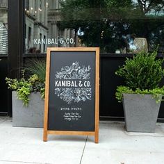 a blackboard sign sitting on the sidewalk in front of a building with potted plants