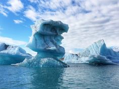 icebergs floating in the water with blue sky and clouds above them, as seen from a boat