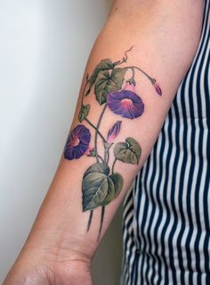 a woman with a tattoo on her arm has a purple flower and leaves growing out of it