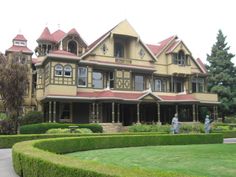 two people are standing in front of a large house with hedges on the side walk