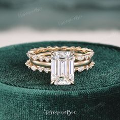 an emerald colored diamond ring sits on top of a green velvet cushion