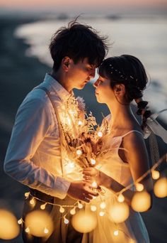 a bride and groom standing next to each other in front of the ocean at sunset