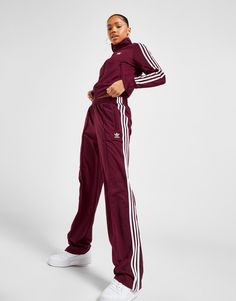 Add some signature sportswear style to your 'drobe with these women's Firebird Track Pants from adidas Originals. Coming in a Shadow Red colourway, these regular-fit track pants are cut from ultra-smooth, lightweight recycled poly fabric with a sleek, shiny finish. They feature an elasticated waistband with a drawcord for a relaxed fit, and wide legs for a laidback, old-school vibe. With zippered side pockets to stash your stuff, they're finished with adidas' legendary 3-Stripes down the sides, and signature Trefoil branding to the thigh. Machine washable. | Our model is 5'7" and wears a size medium. | IB7327 Burgundy Adidas, Tracksuit Outfit, Adidas Tracksuit, Adidas Joggers, Adidas Track Pants, Adidas Outfit, Adidas Track, Red Adidas, Pink Adidas