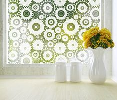 two white vases with yellow flowers in front of a patterned wallpapered window