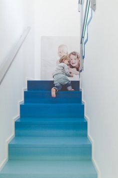 a blue staircase leading up to a white wall with a photo on the stair rail