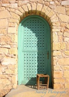 a wooden chair sitting in front of a stone building with a green door and window