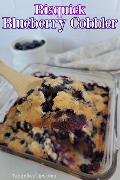 a blueberry cobbler in a glass dish with a wooden spoon on the side