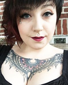 a close up of a person with tattoos on her chest and breast piercings in front of a brick wall